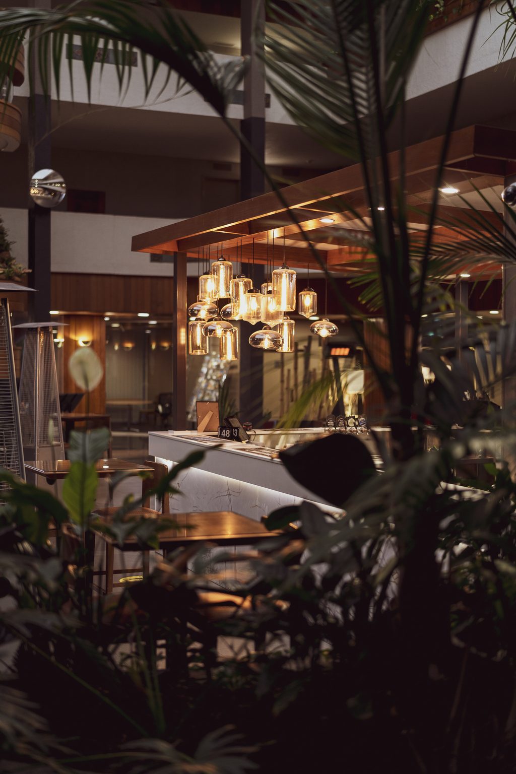 Clusters of amber pendant lights hang over a bar counter, seen through dark palm fronds in the foreground.