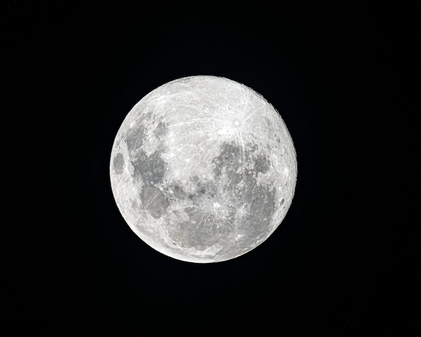 A full moon fills the frame against black sky, its craters and bright ray systems sharp across the face.